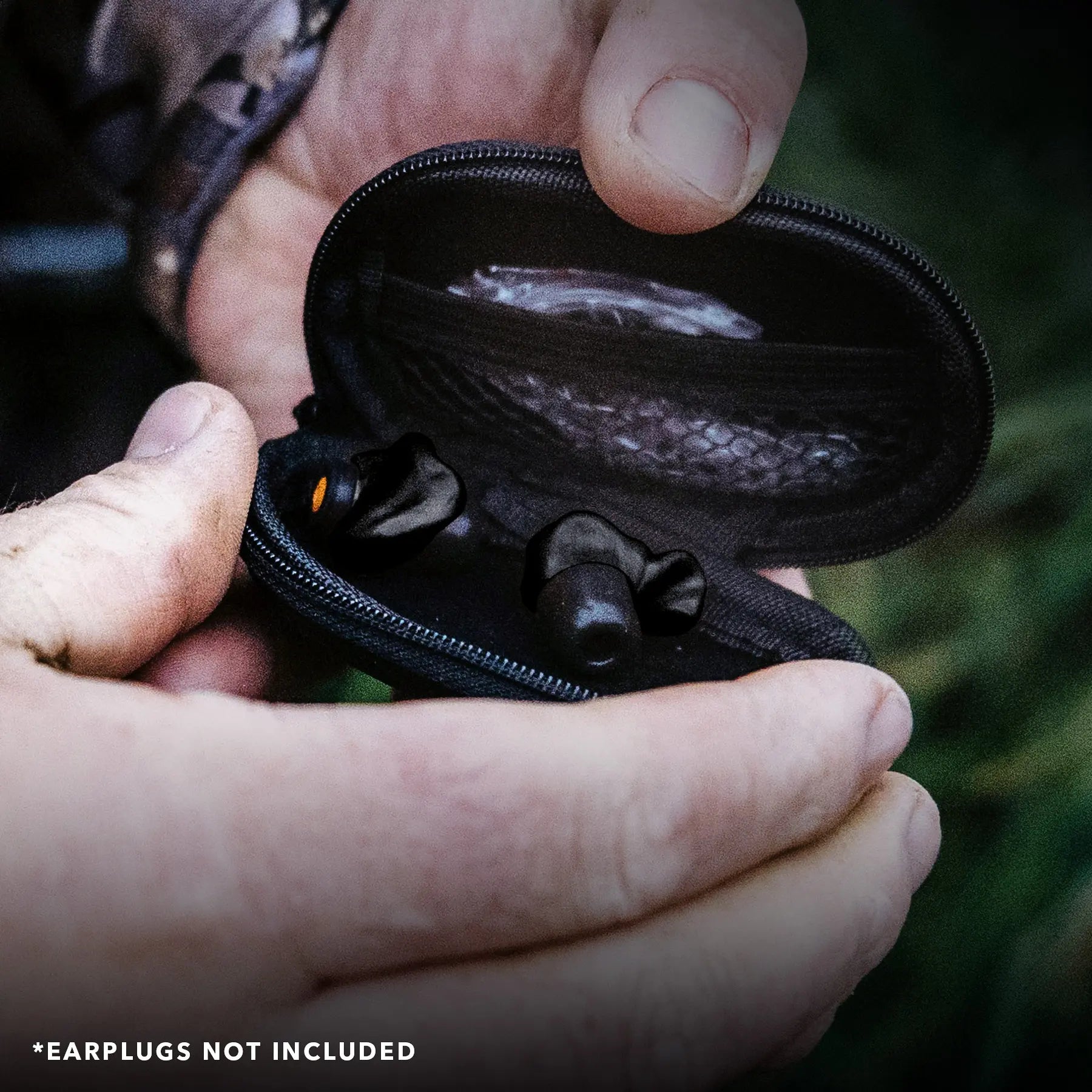 A person is holding a black earphones case with a premium zipper, containing custom-molded earplugs. The case is open, revealing a mesh pocket inside. The background is blurred, showing an outdoor setting. Text at the bottom states, "*EARPLUGS NOT INCLUDED.
Product Name: Premium Earplug and Earphone Carrying Case
Brand Name: Decibullz